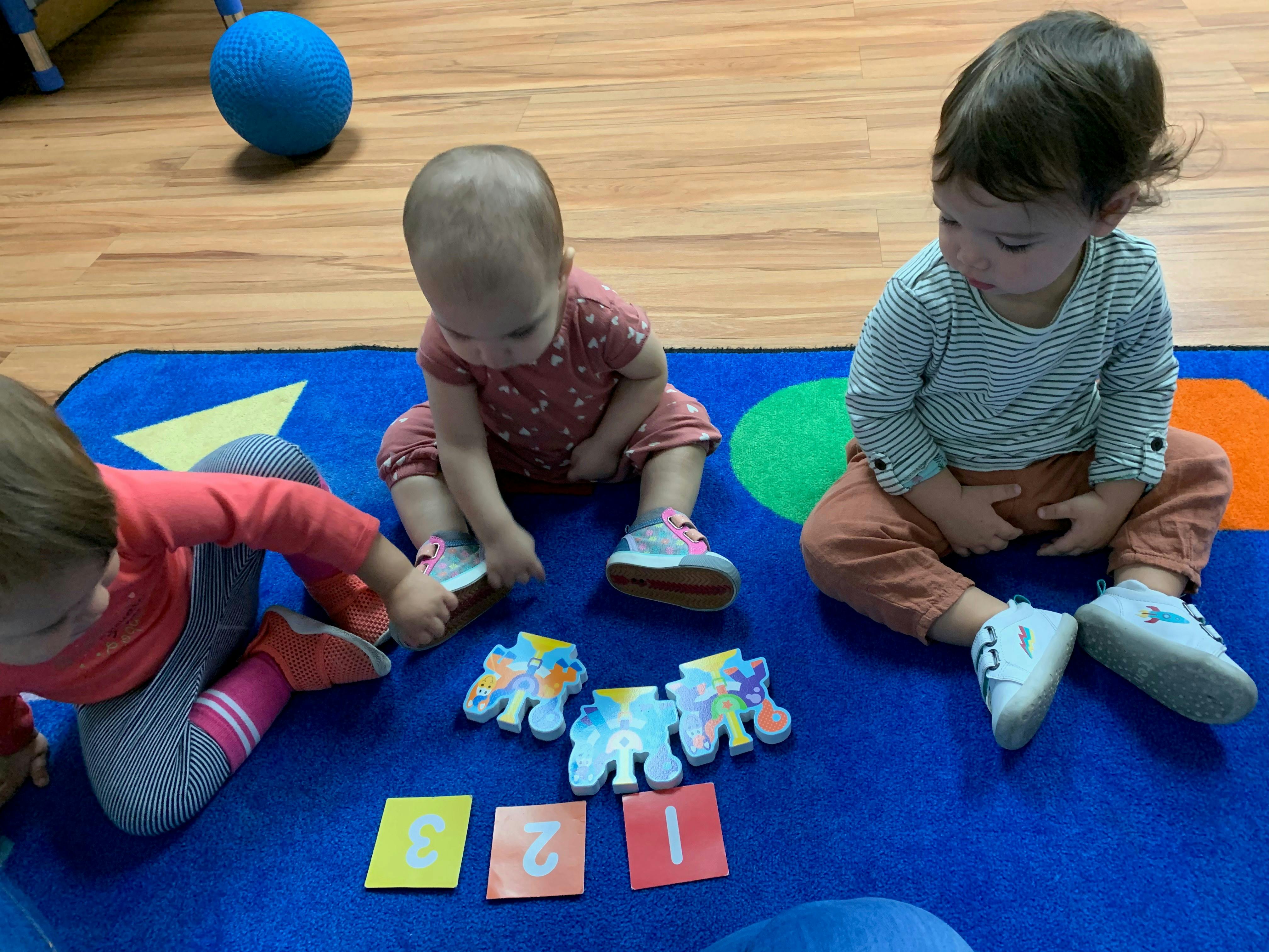 Three children playing with number cards and toy elephants on a blue mat