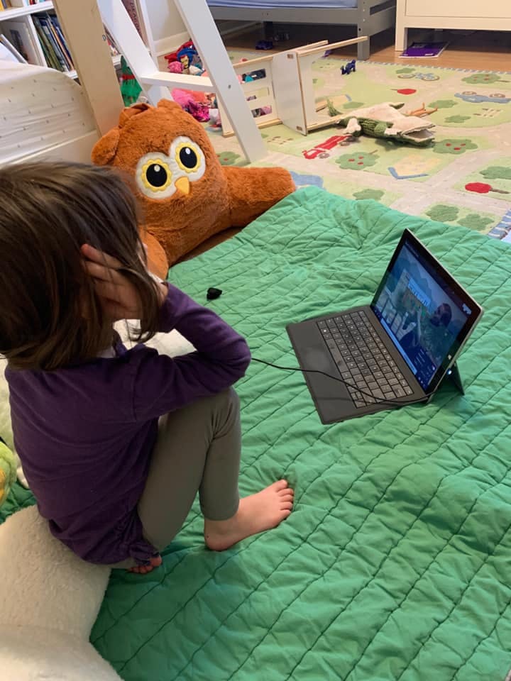 Child sitting on floor watching laptop with stuffed owl