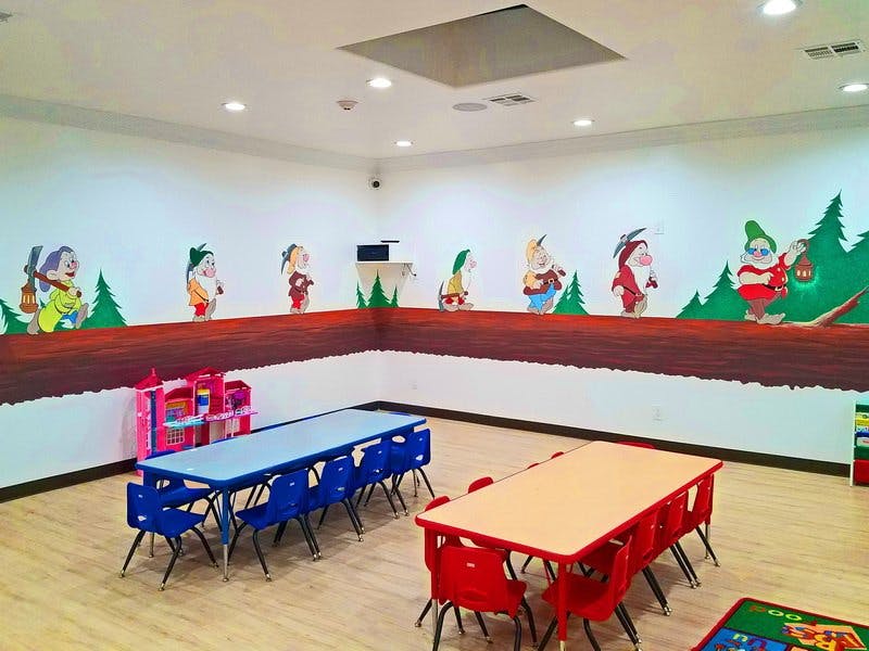 Classroom with small tables and chairs, wall murals of cartoon characters