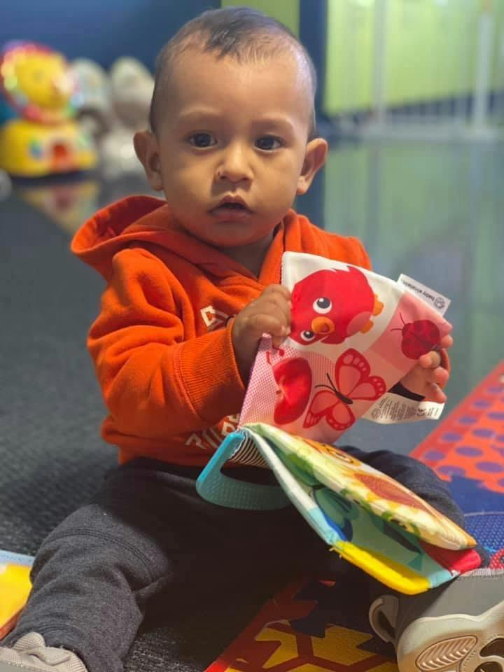 Child in orange hoodie holding a soft book with a red bird and butterflies
