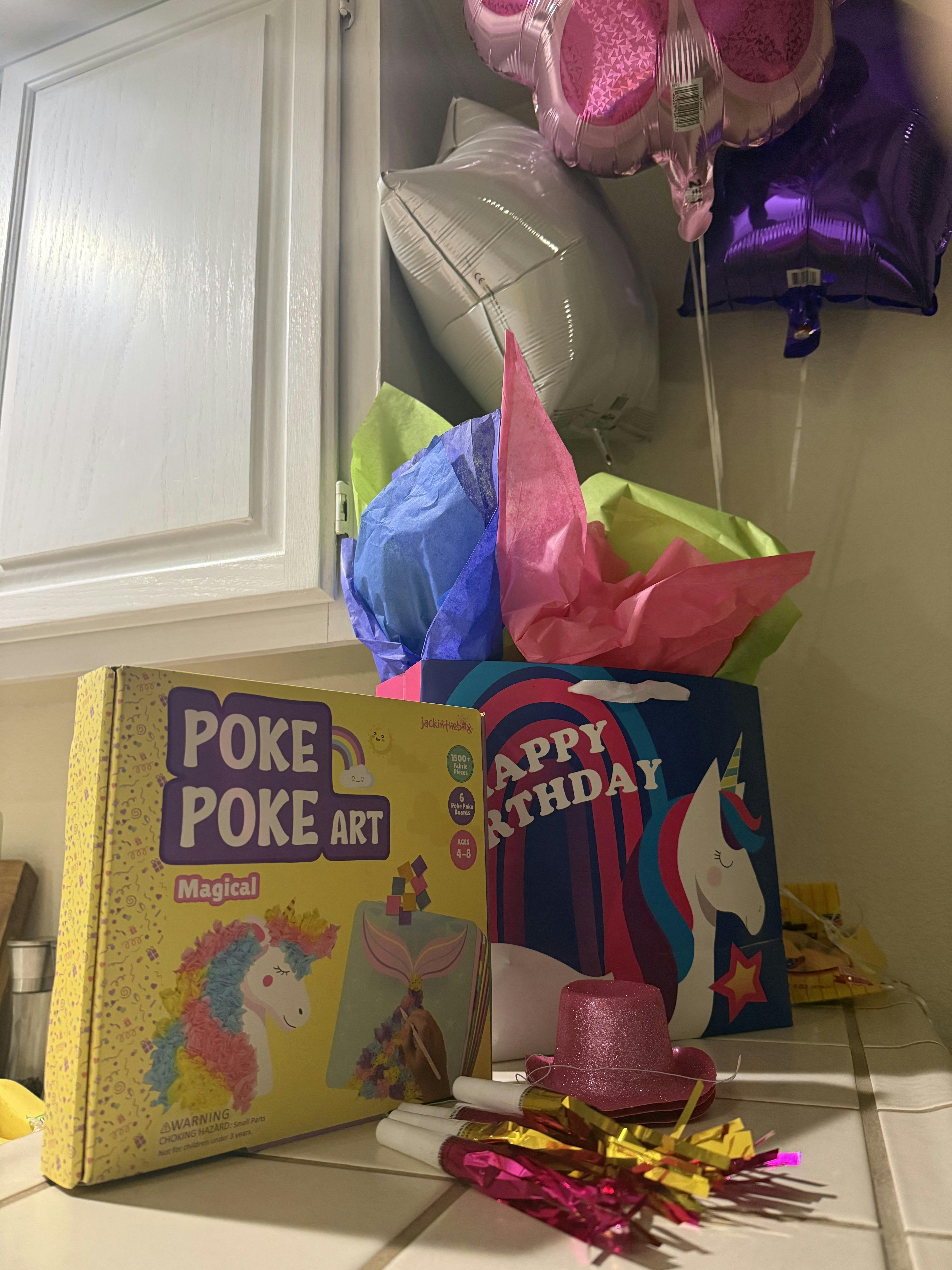Birthday party setup with a Poke Poke Art box, gift bag, and balloons