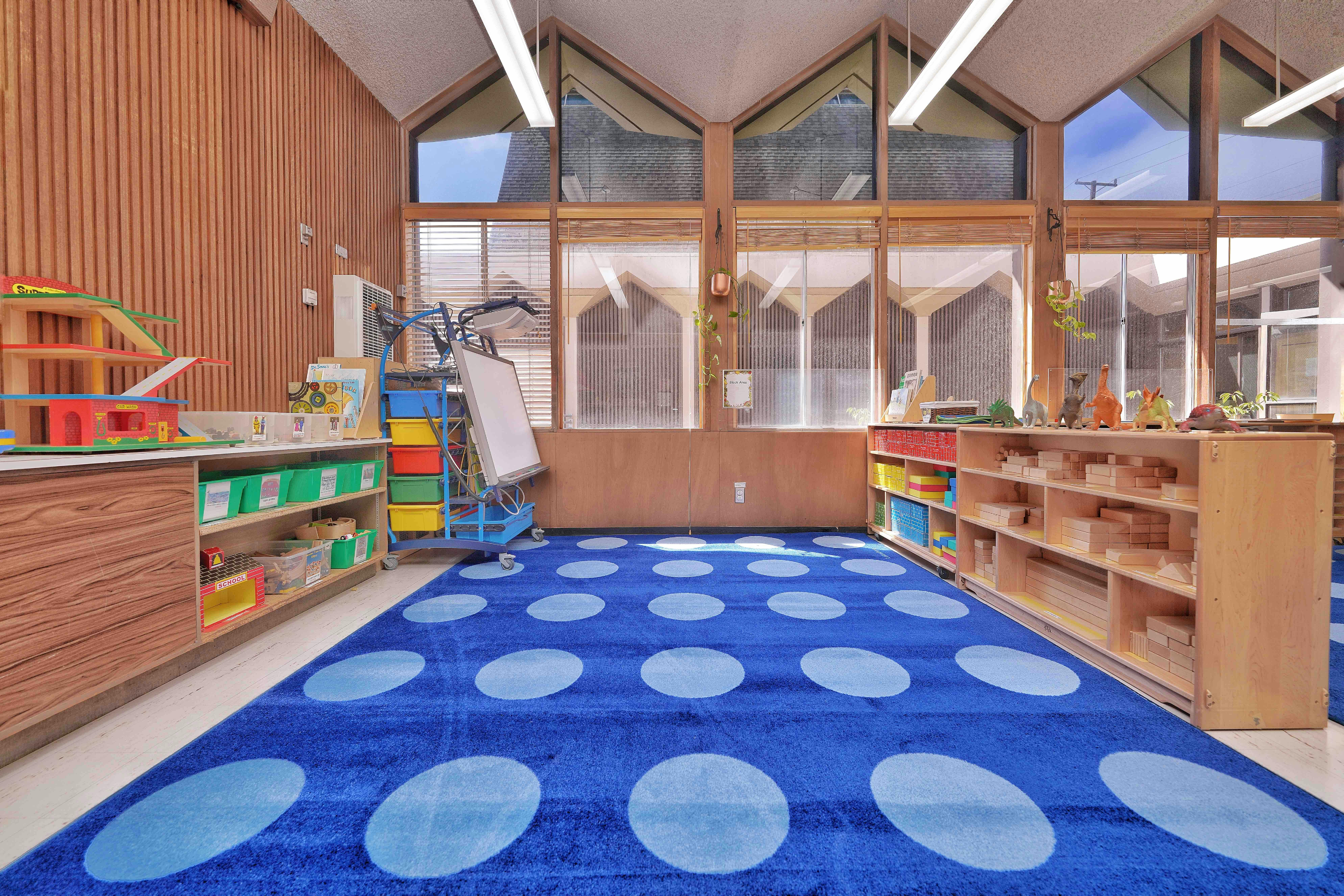 Classroom with wooden shelves, toys, and a blue rug with polka dots