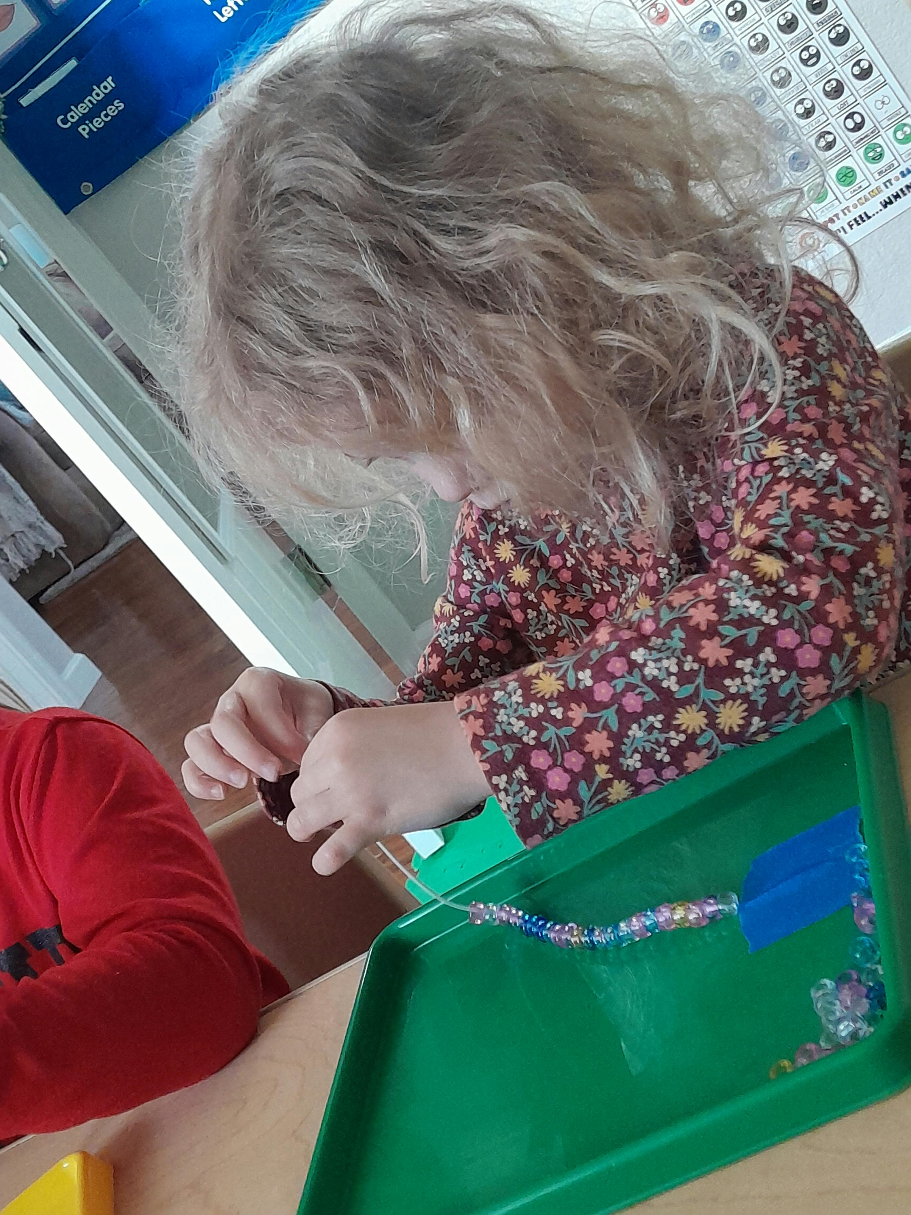 Child with curly hair stringing beads on a tray