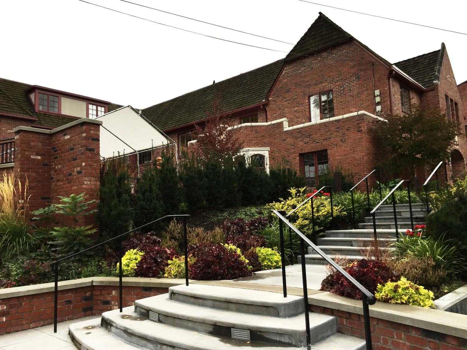 Brick building with multiple windows and gabled roofs, concrete stairs with handrails