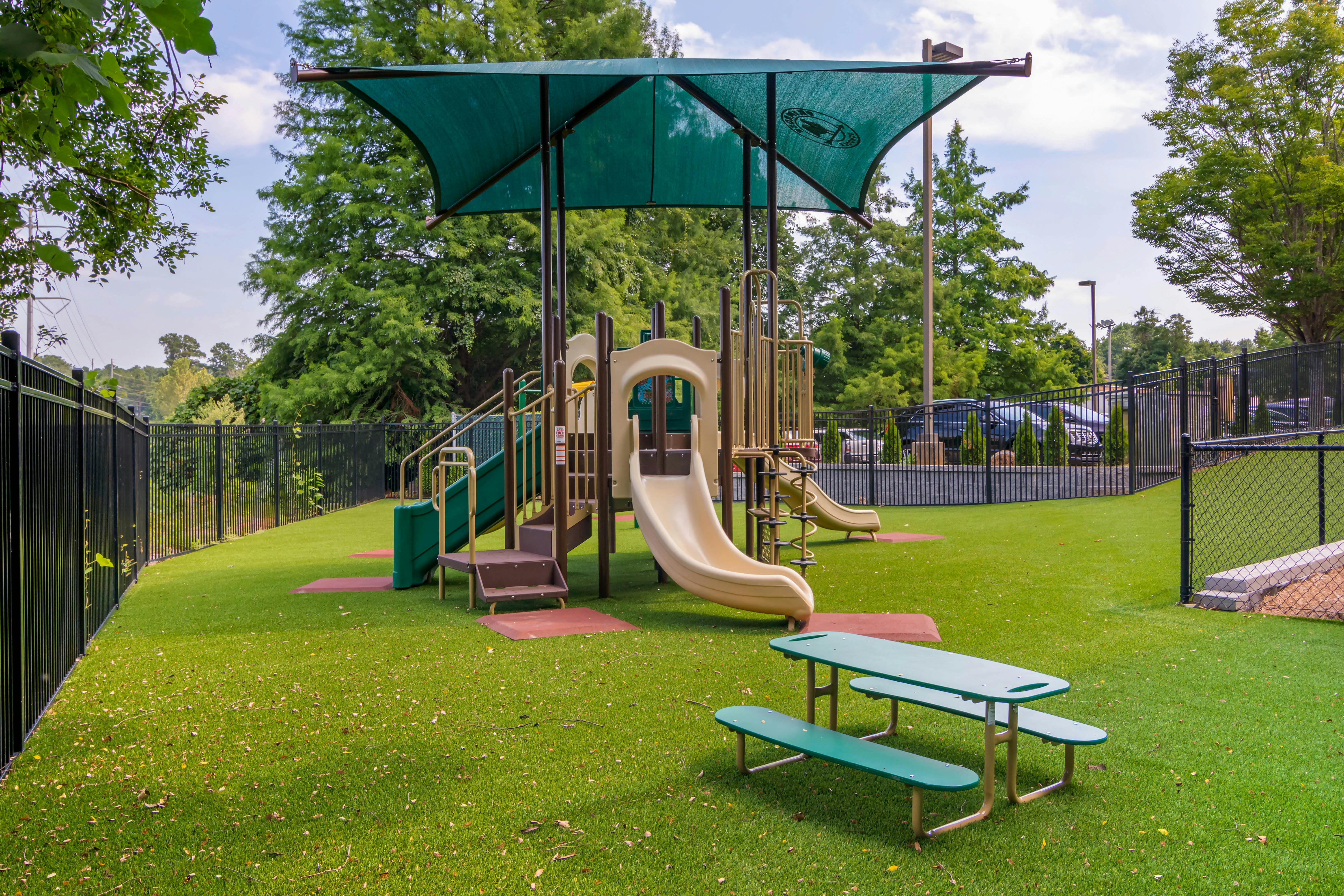 Playground with slides, stairs, and a green shade cover over artificial turf