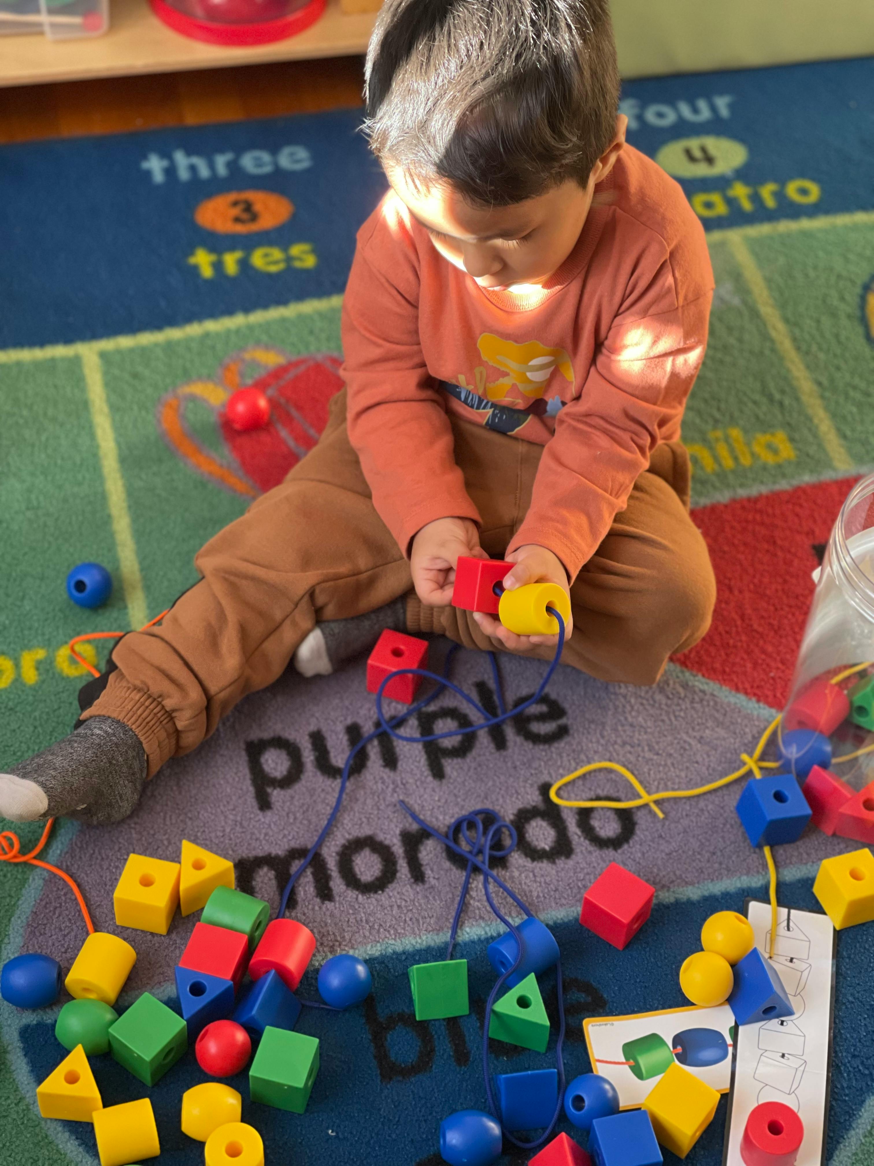Child playing with lacing beads on a colorful rug