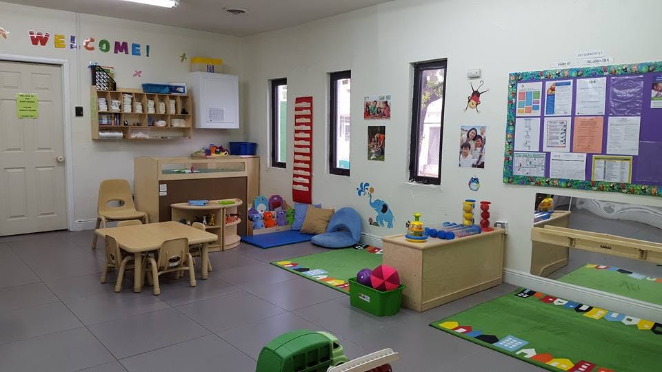 Classroom with small tables and chairs, play mats, and bulletin boards