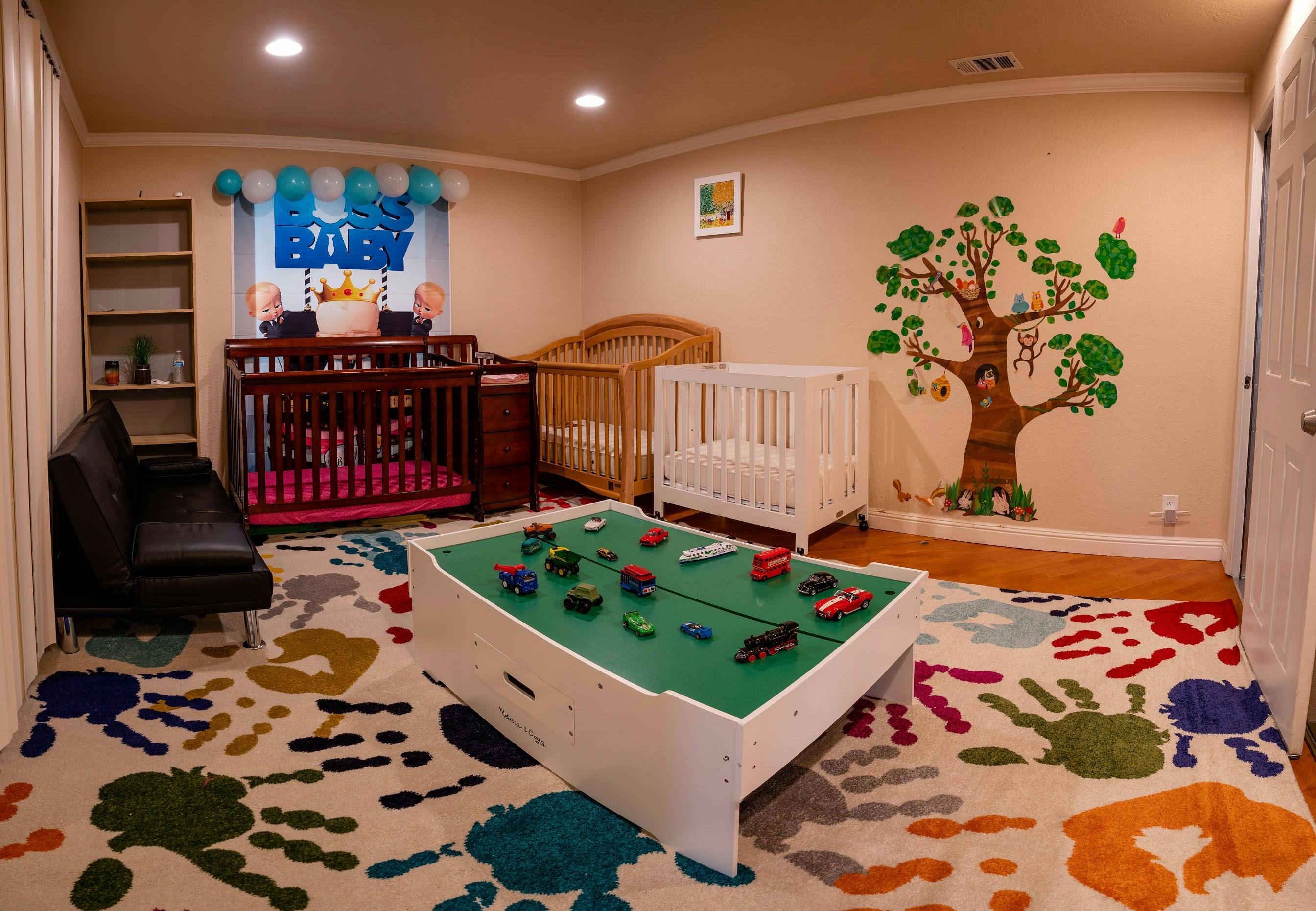 Nursery room with multiple cribs, a play table, and a colorful rug