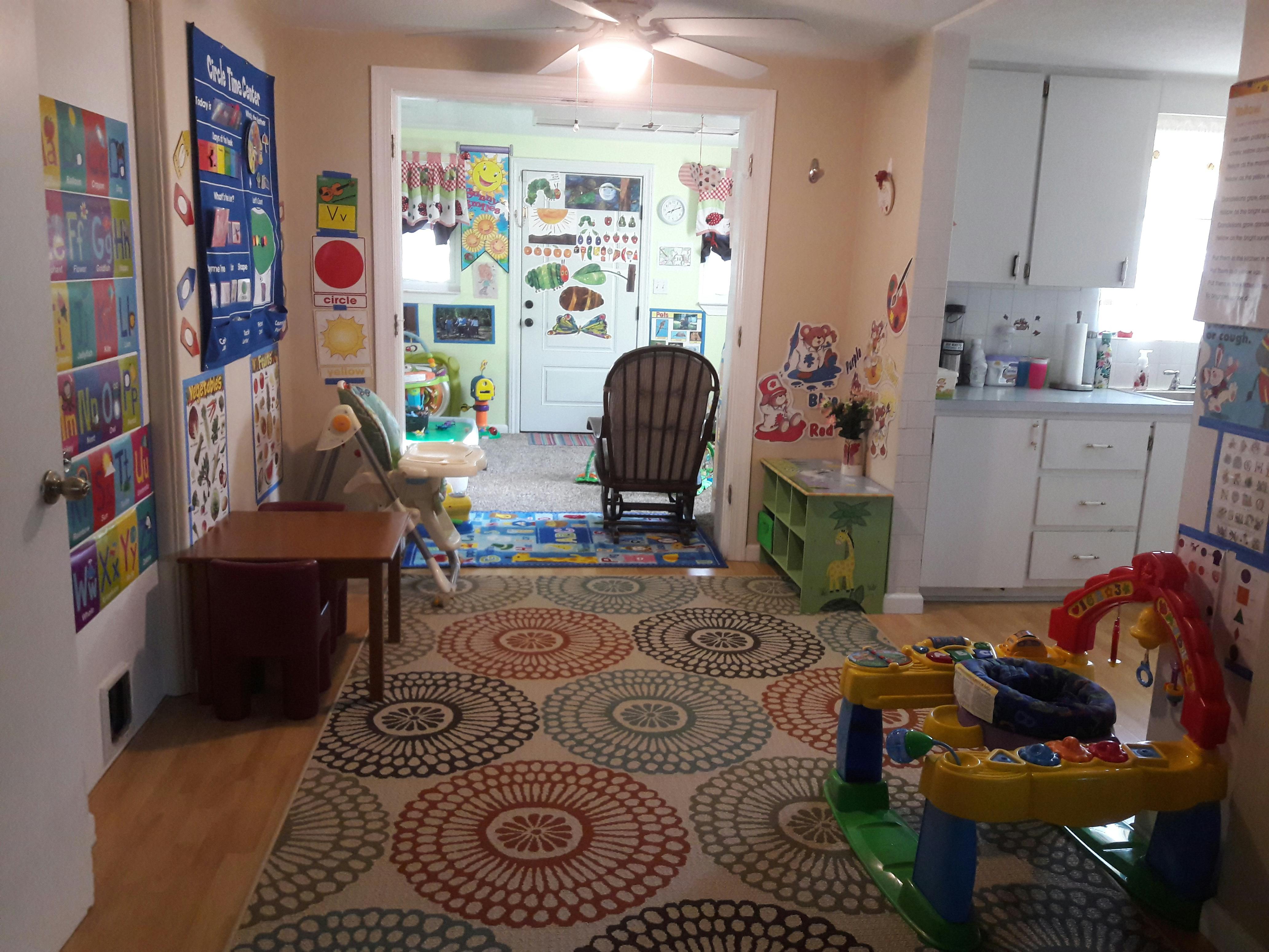 Playroom with colorful rug, toys, and view into kitchen