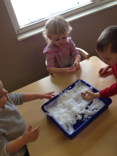 Three children playing with white fluffy material in a blue tray