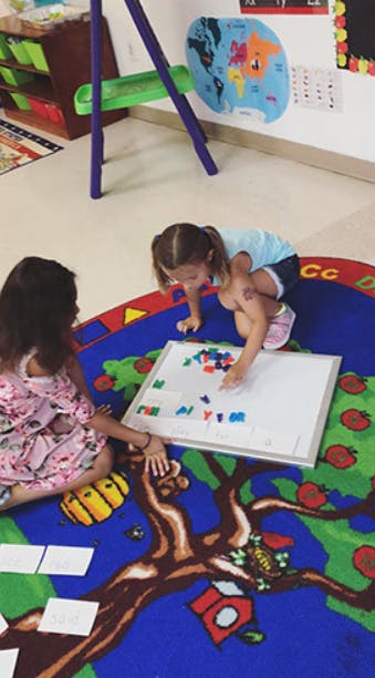 Two children playing with magnetic letters on a whiteboard in a classroom