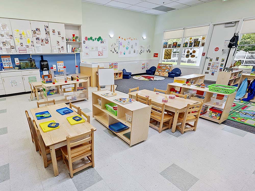 An empty classroom with small tables and chairs, shelves, and artwork on the walls