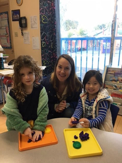 Adult and two children playing with purple play-doh in a classroom