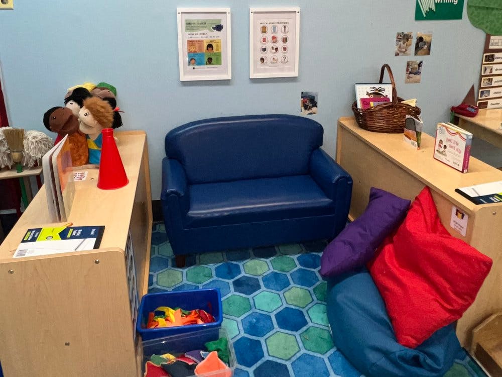 Children's classroom corner with a small blue couch, pillows, and puppets
