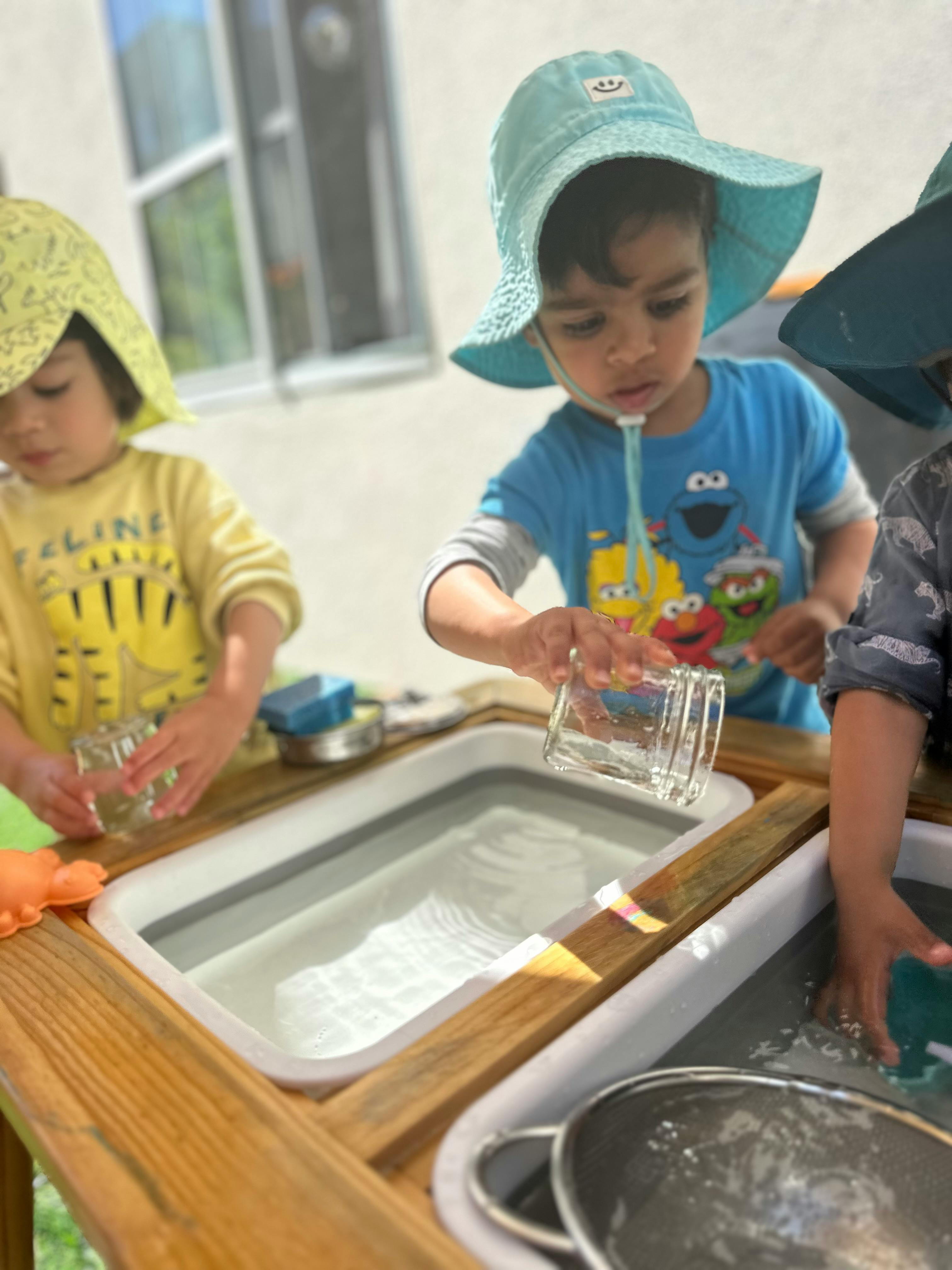Child pouring water from a glass into a bin, with another child nearby