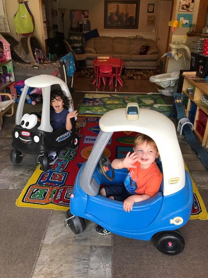 Two children in toy cars on a rug