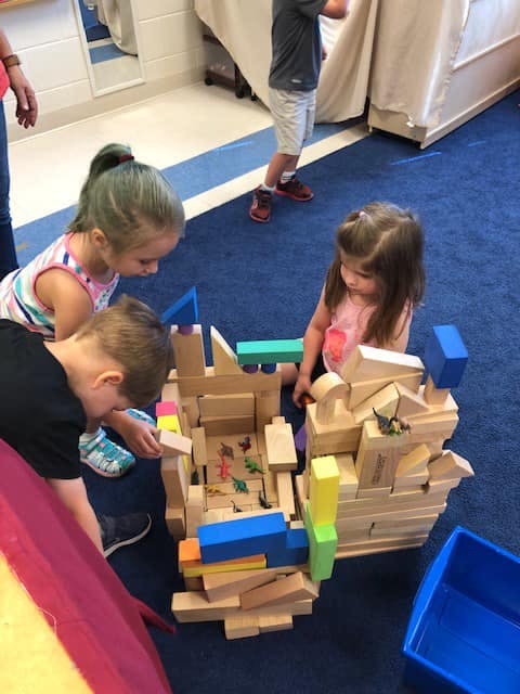 Three children playing with wooden blocks on a blue carpet