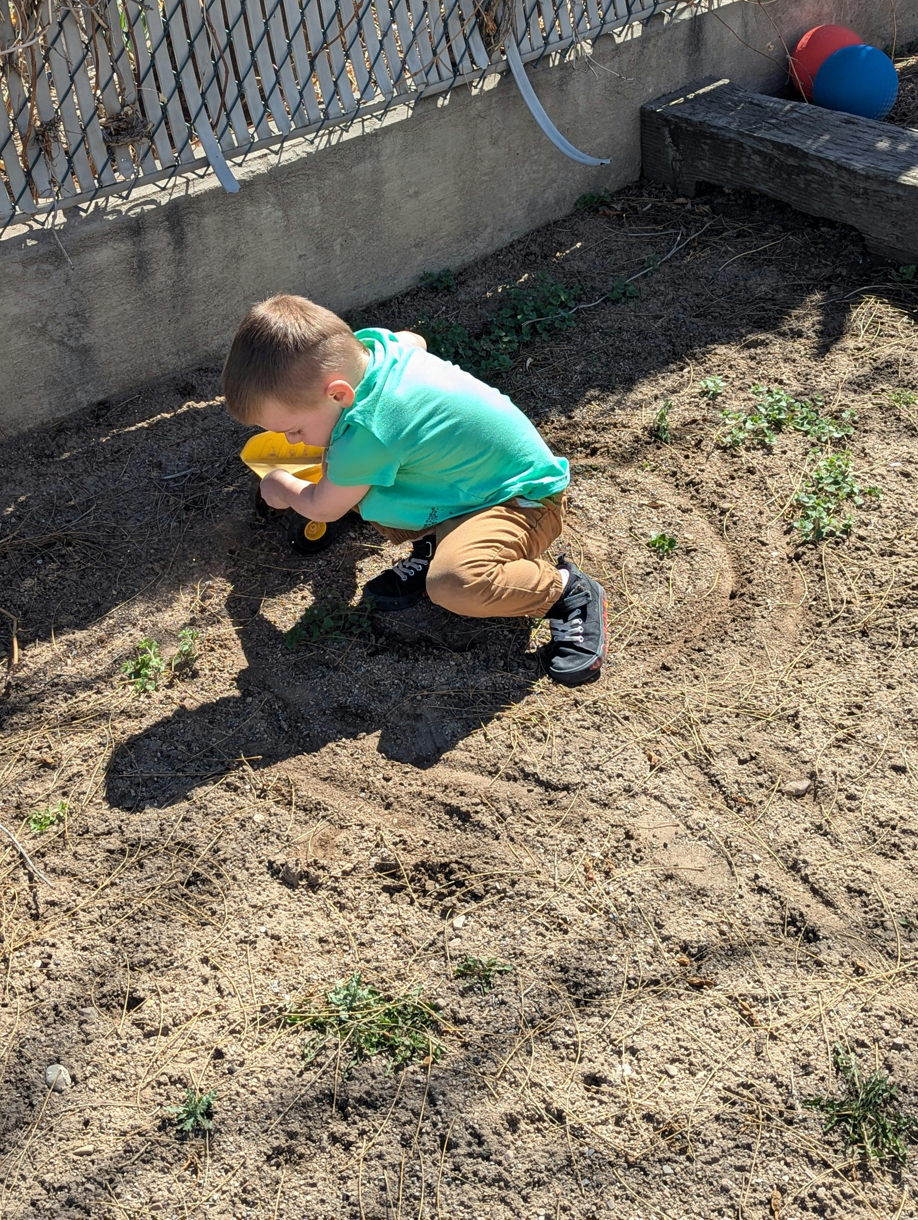 Child kneeling on dirt ground playing with a yellow toy