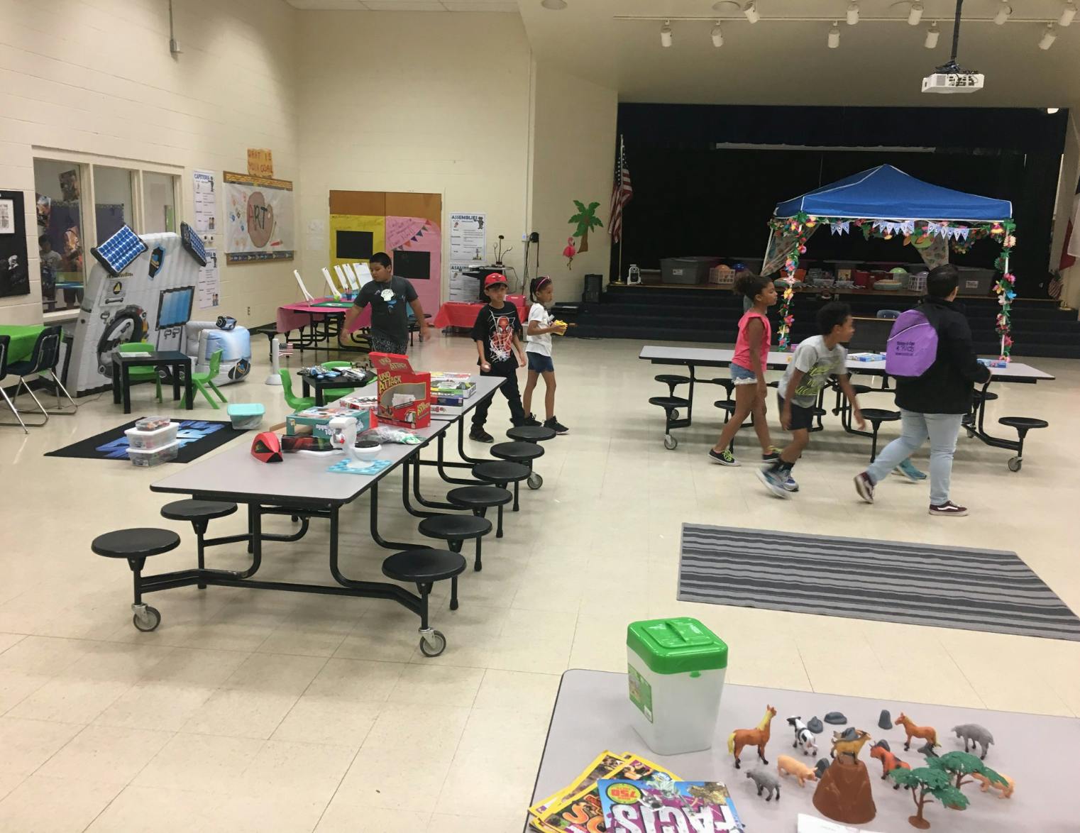 Children and teens walking in a large room with tables and a stage