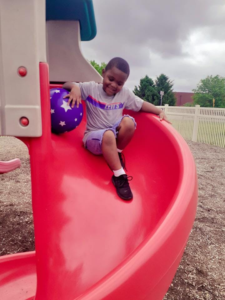 Child on a red slide holding a purple ball
