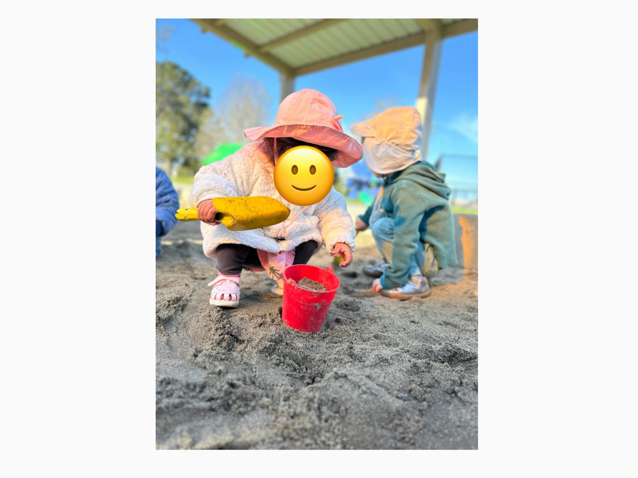 Two children playing in a sandbox with a bucket and shovel