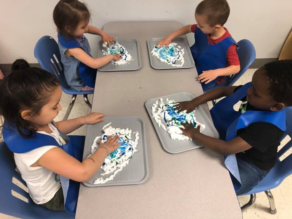 Four children playing with shaving cream and paint at a table