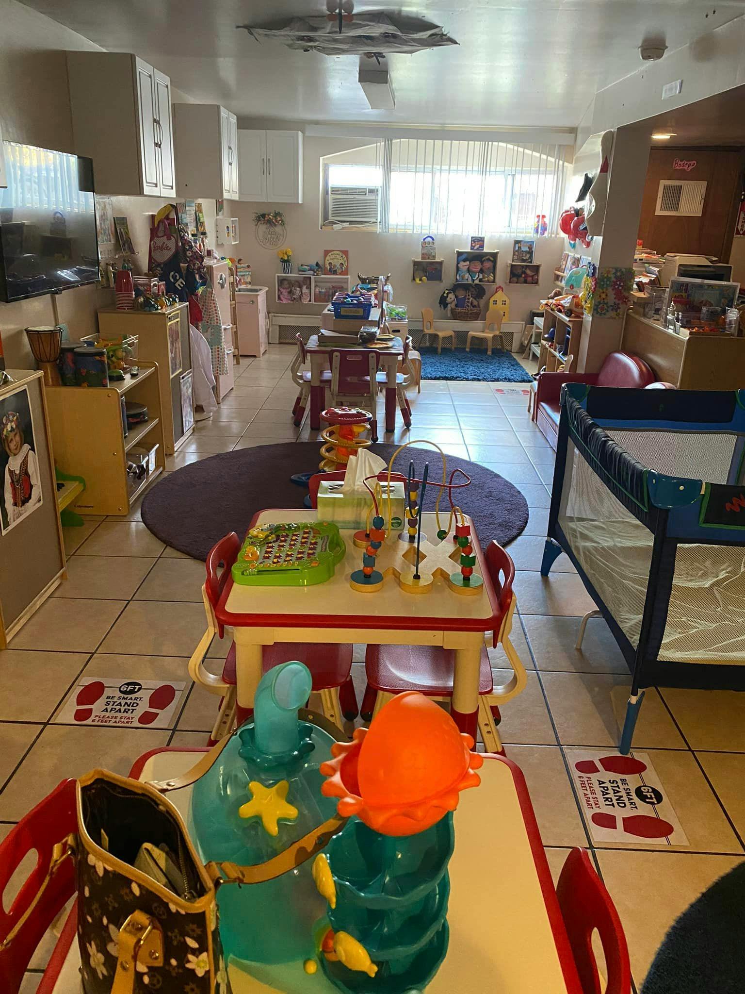 A room with multiple small tables and chairs, a crib, and toys