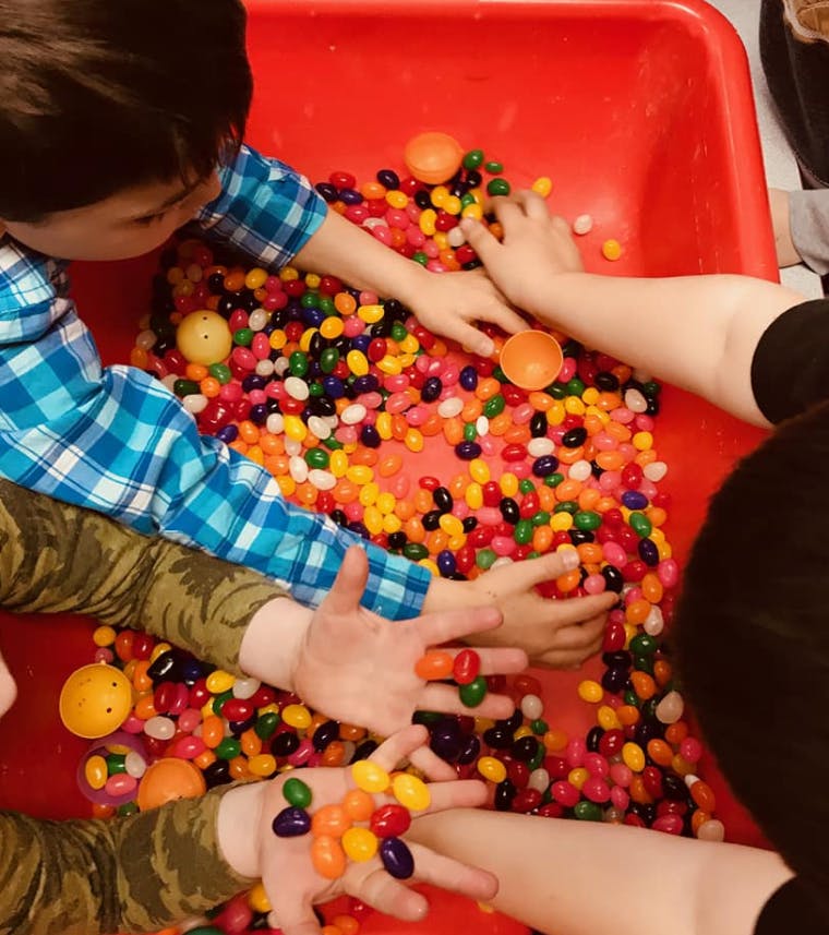 Multiple hands reaching into a bin of colorful jelly beans