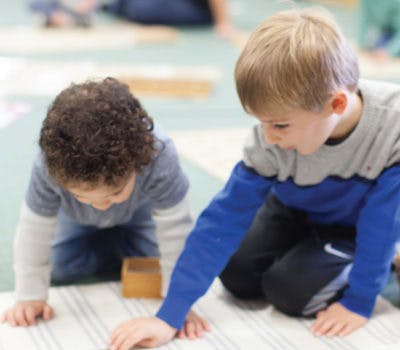Two children kneeling on a mat, looking down at an object