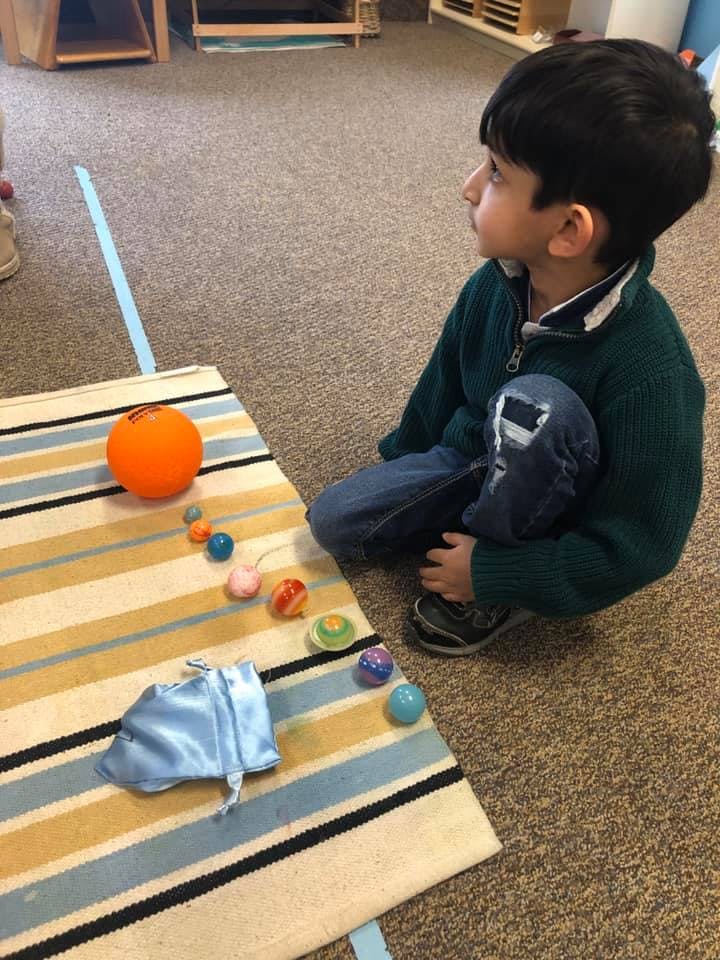 Child kneeling on floor next to a striped mat with toys