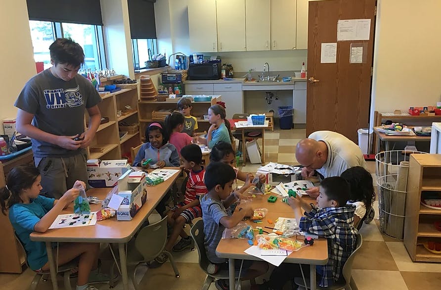 Adults and children working at tables in a classroom