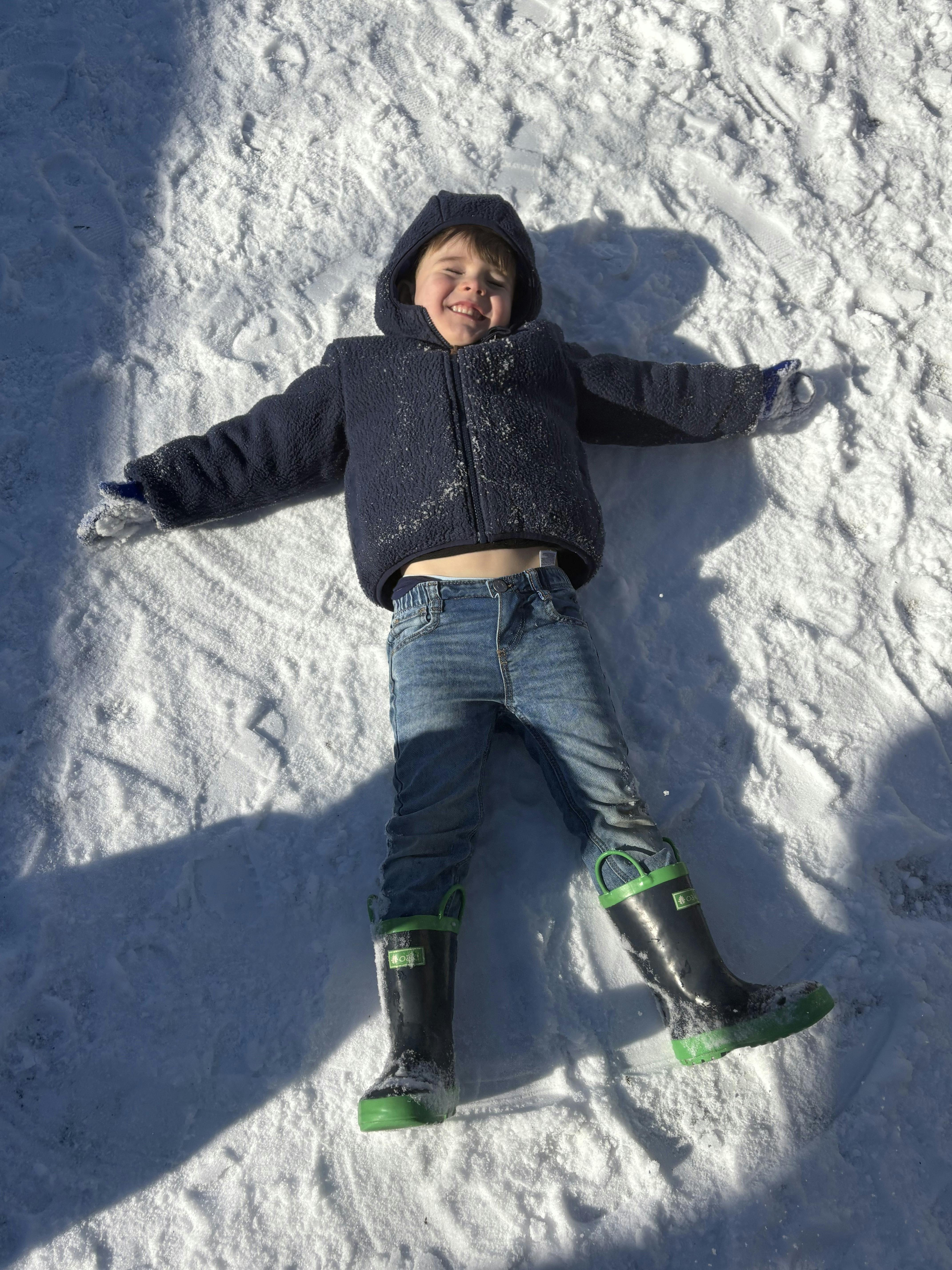 Child lying on their back in the snow making a snow angel