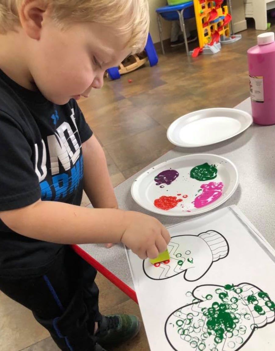 Child painting a mitten outline with a sponge