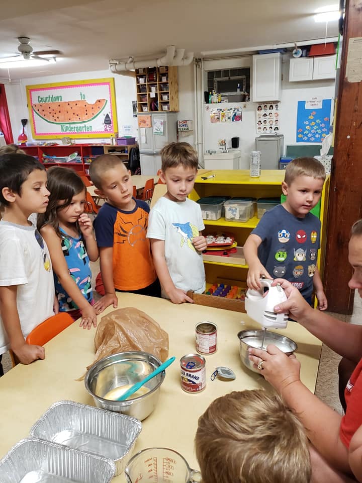 Children watching an adult use a hand mixer to prepare food