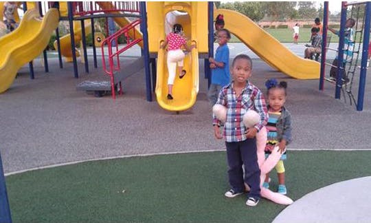 Two children standing on playground, another child climbing up a slide