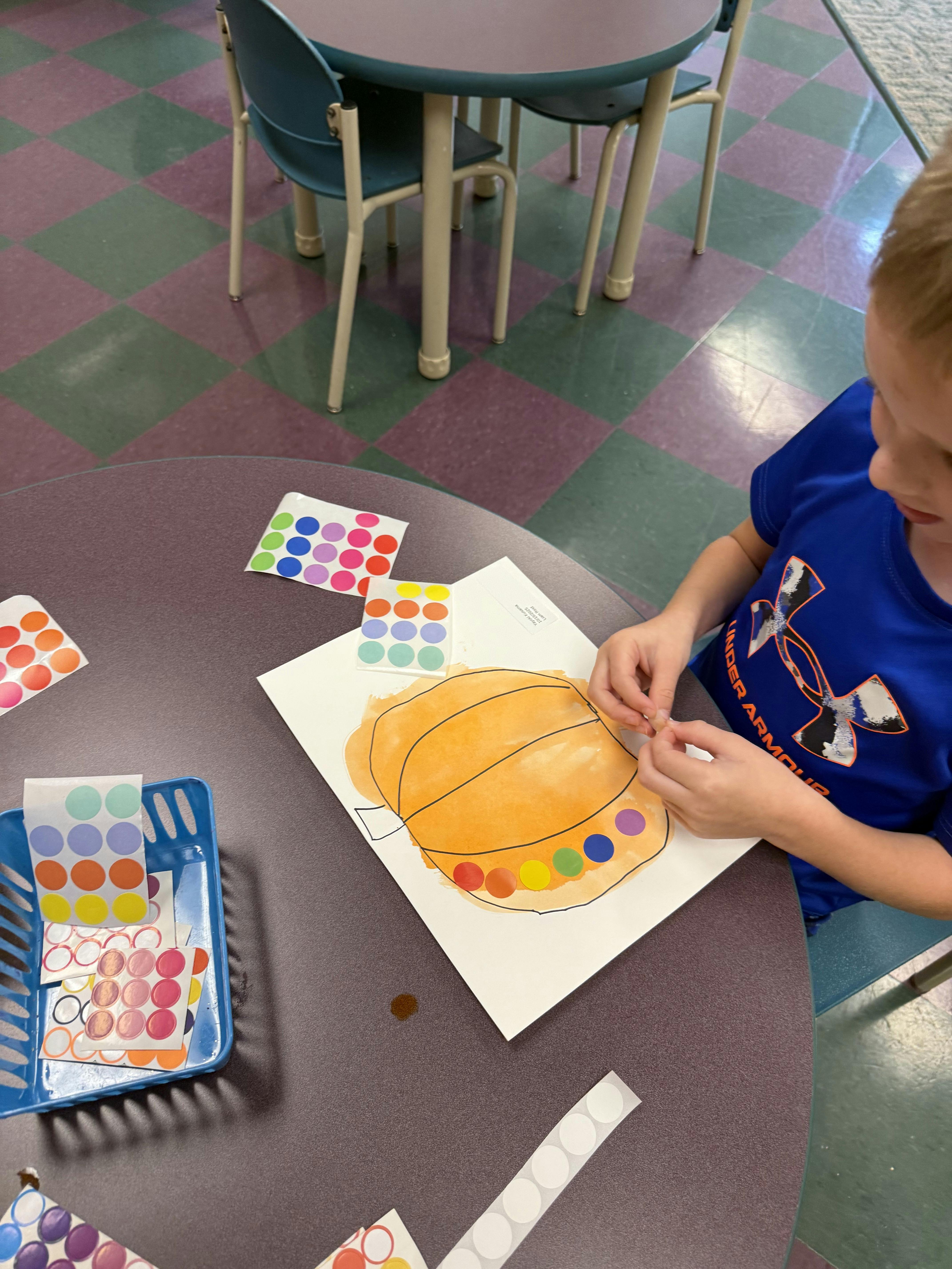 Child placing colorful round stickers on a pumpkin drawing