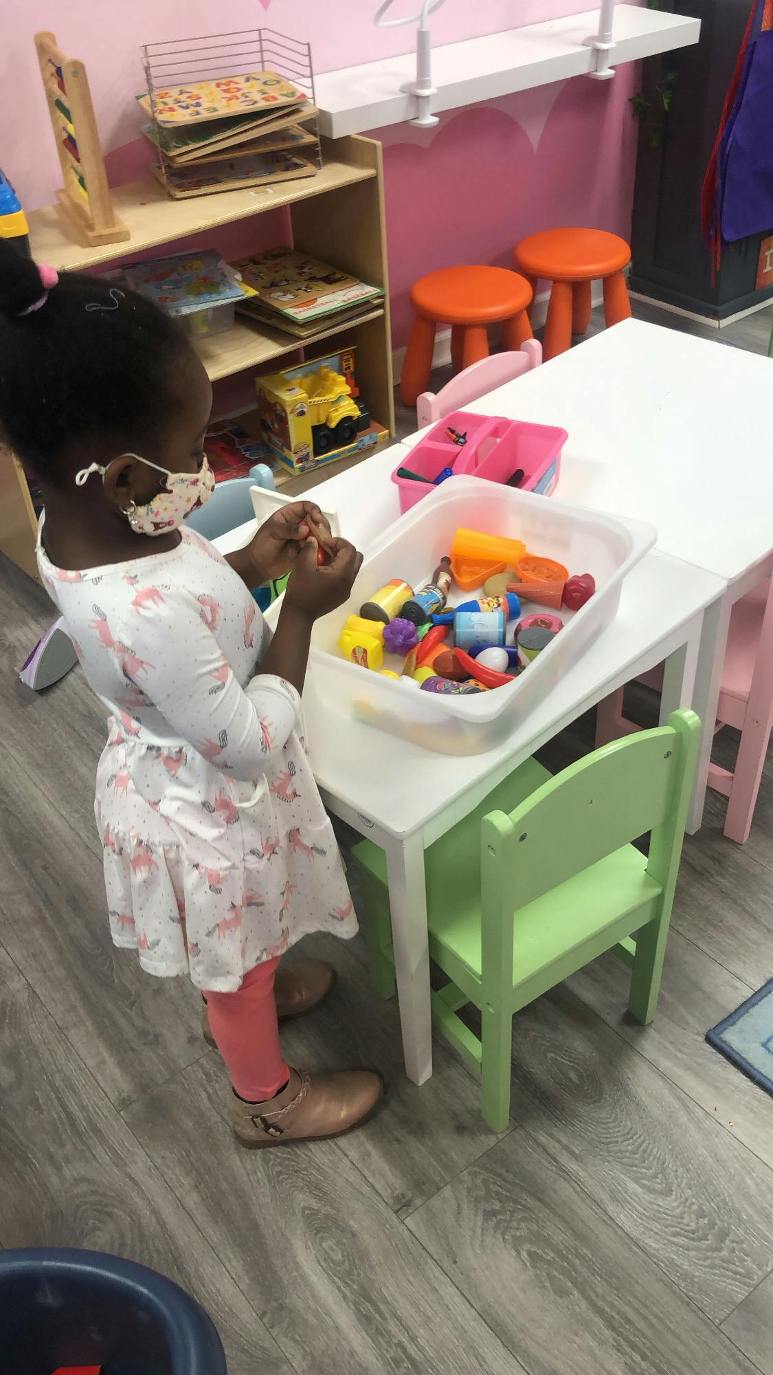Child in a mask playing with toys at a table