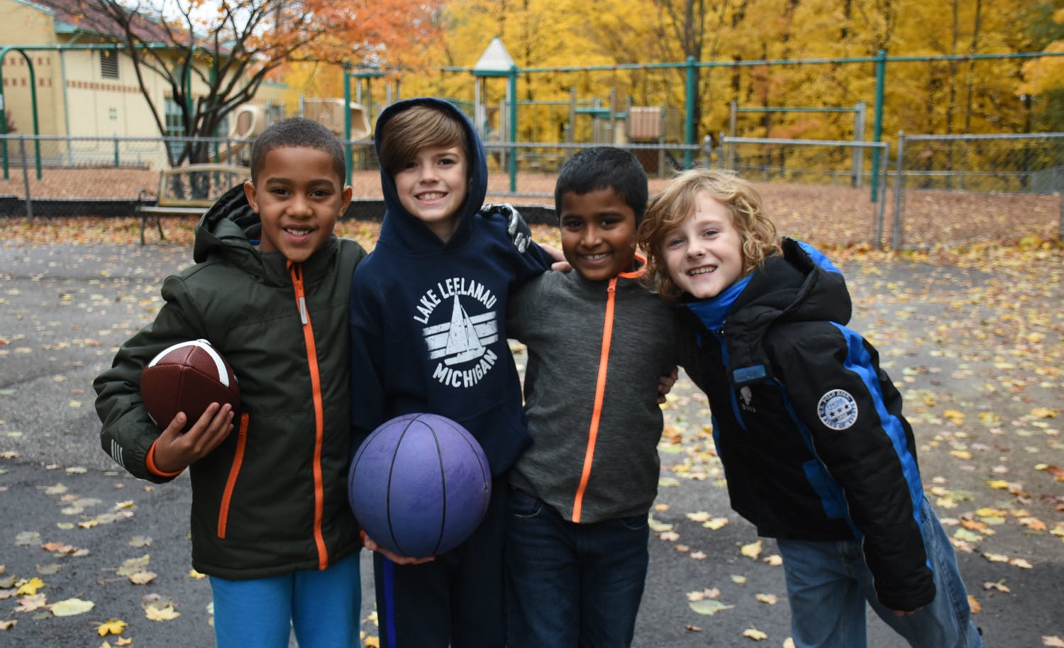 Four children holding a football and a basketball outdoors