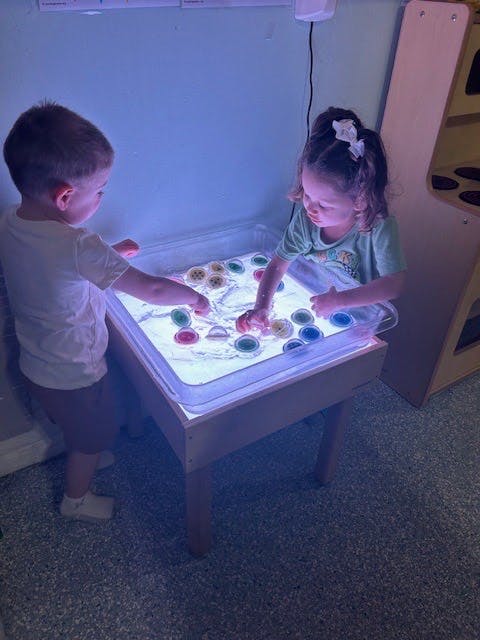 Two children playing with colorful objects on a light table