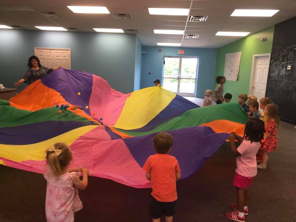 Adult and children playing with a large colorful parachute indoors