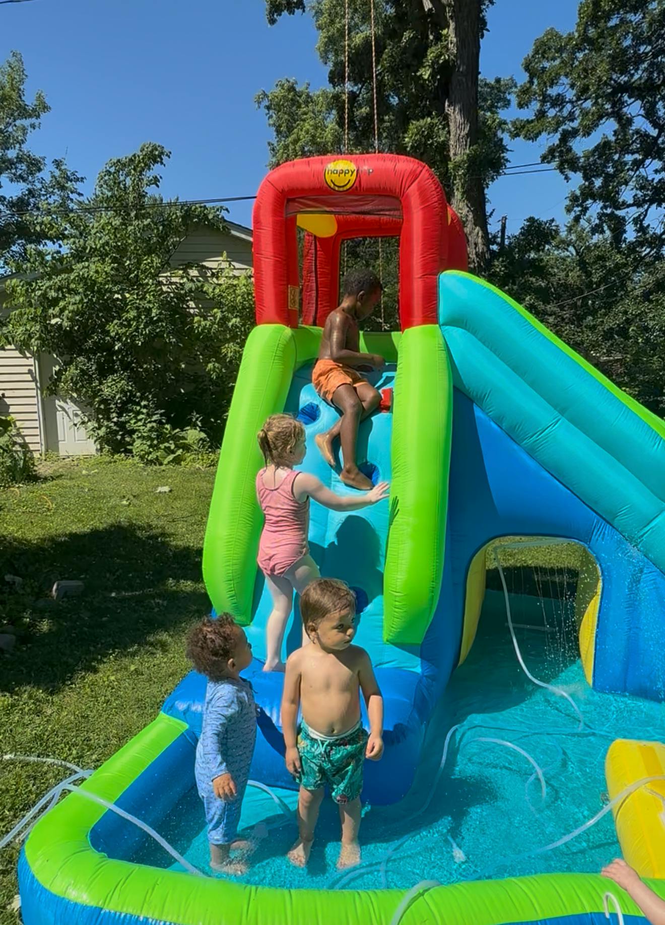 Children playing on a colorful inflatable water slide in a backyard