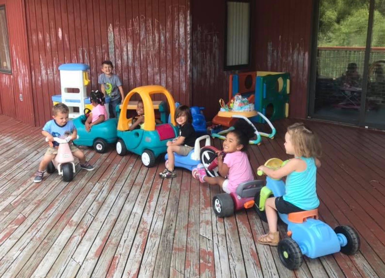 Children playing with ride-on toys on a wooden deck