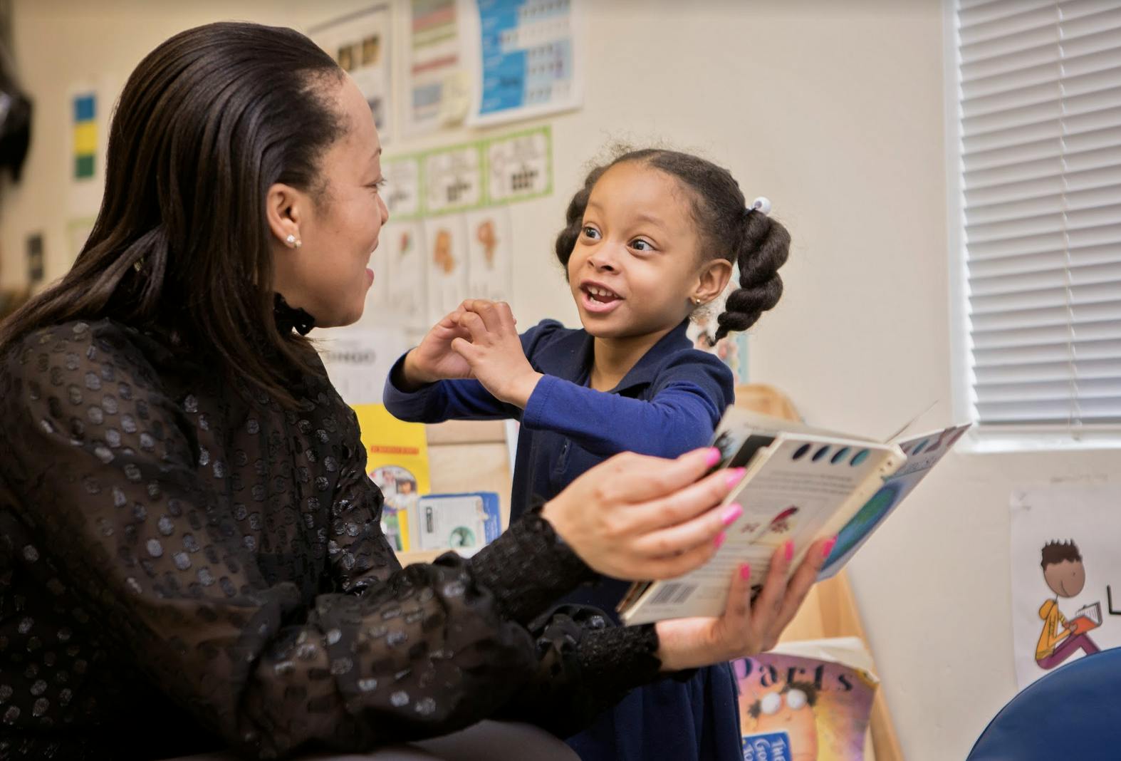 Adult holding a book and child talking in pigtails talking in a classroom