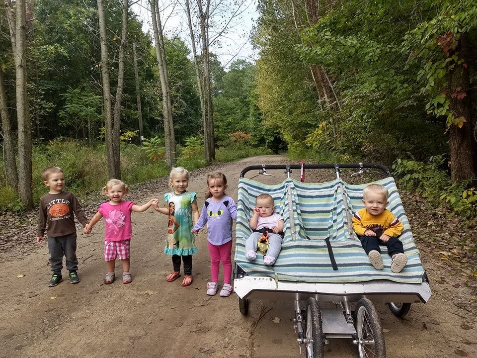 Children standing on a path next to a multi-seat stroller with two babies