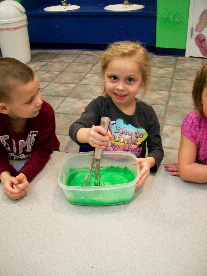 Child whisking green mixture in a container, with another child watching