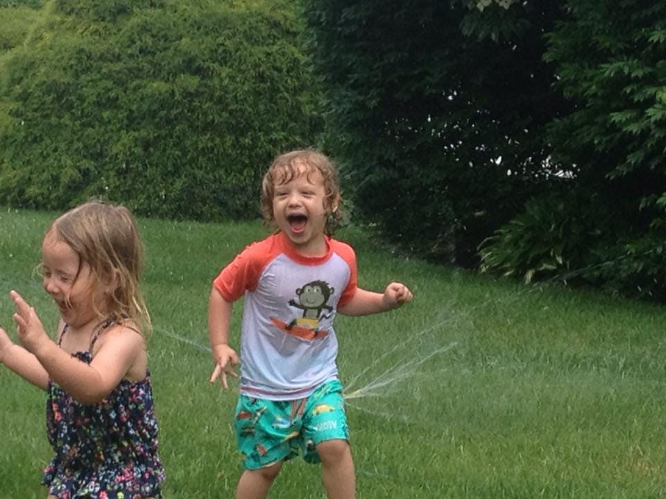 Two children playing in a sprinkler on a grassy lawn