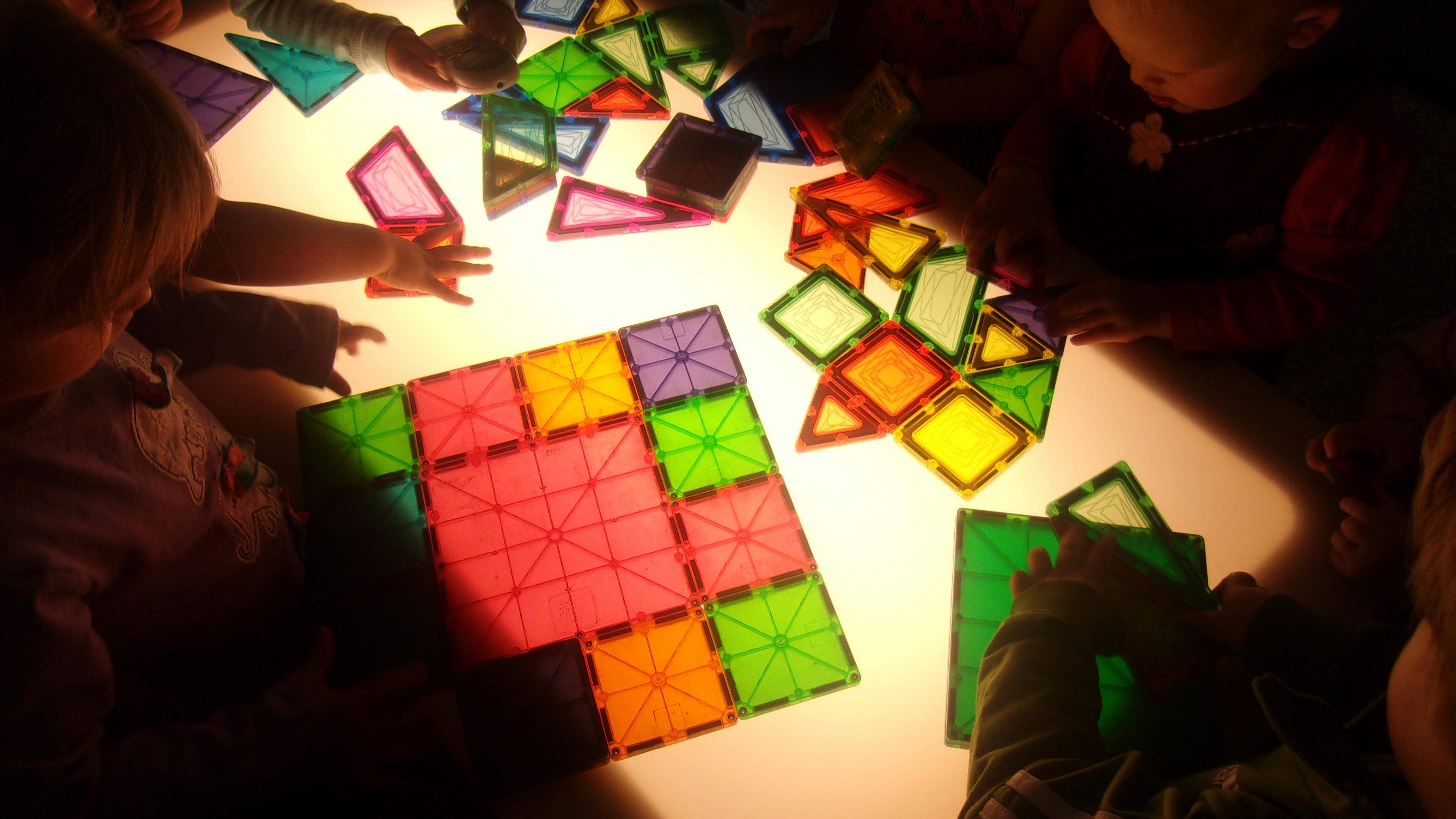 Children playing with colorful translucent magnetic tiles on a light table