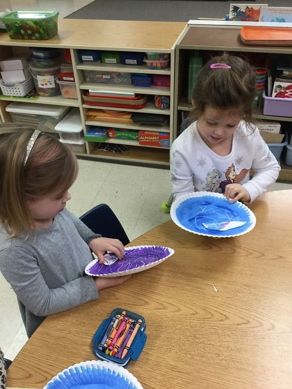 Two children making crafts with paper plates at a table