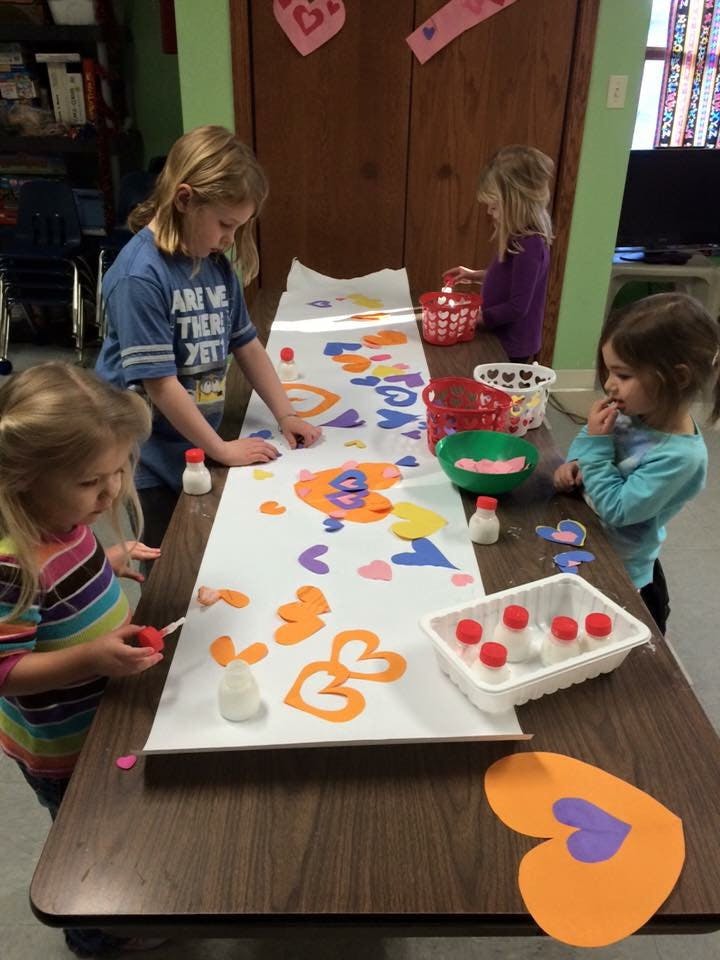 Three children decorating a long paper with heart cutouts