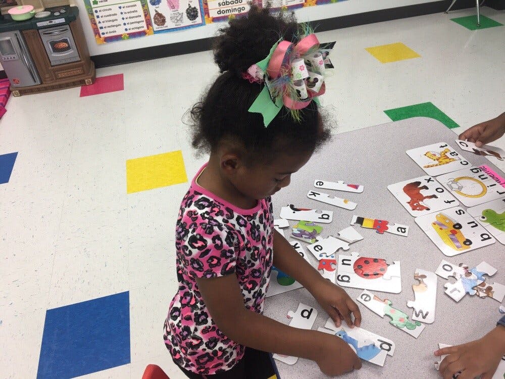 Child playing with alphabet cards at a table in a classroom